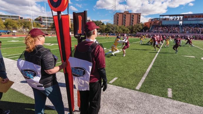 丹尼斯Ugolini and Jennifer Steele watch a 澳门金沙线上赌博官网 Football game from the sidelines with the down and distance markers