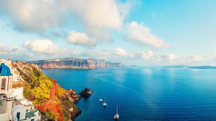 View of ocean, coastline, and blue-roofed buildings in Greece